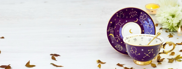 Purple tea leaf reading teacup and saucer with gold spoon. Gold astrology images on cup and saucer.
