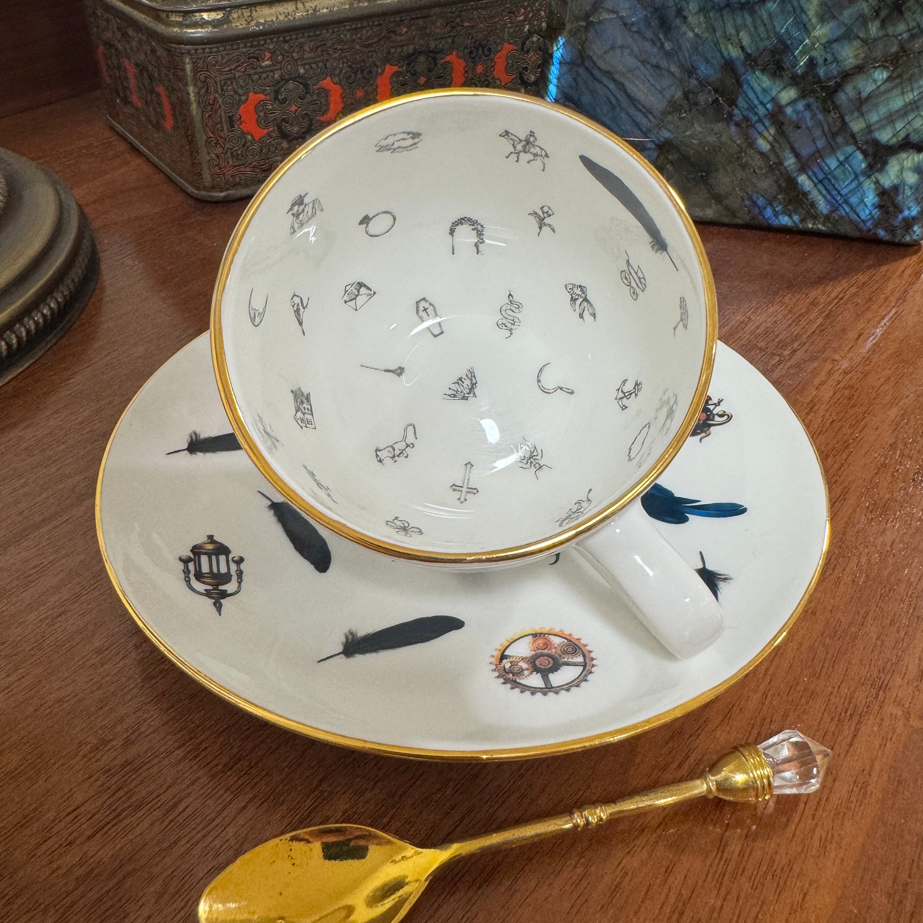 Teacup with decorative interior, saucer, and gold spoon on a wooden surface