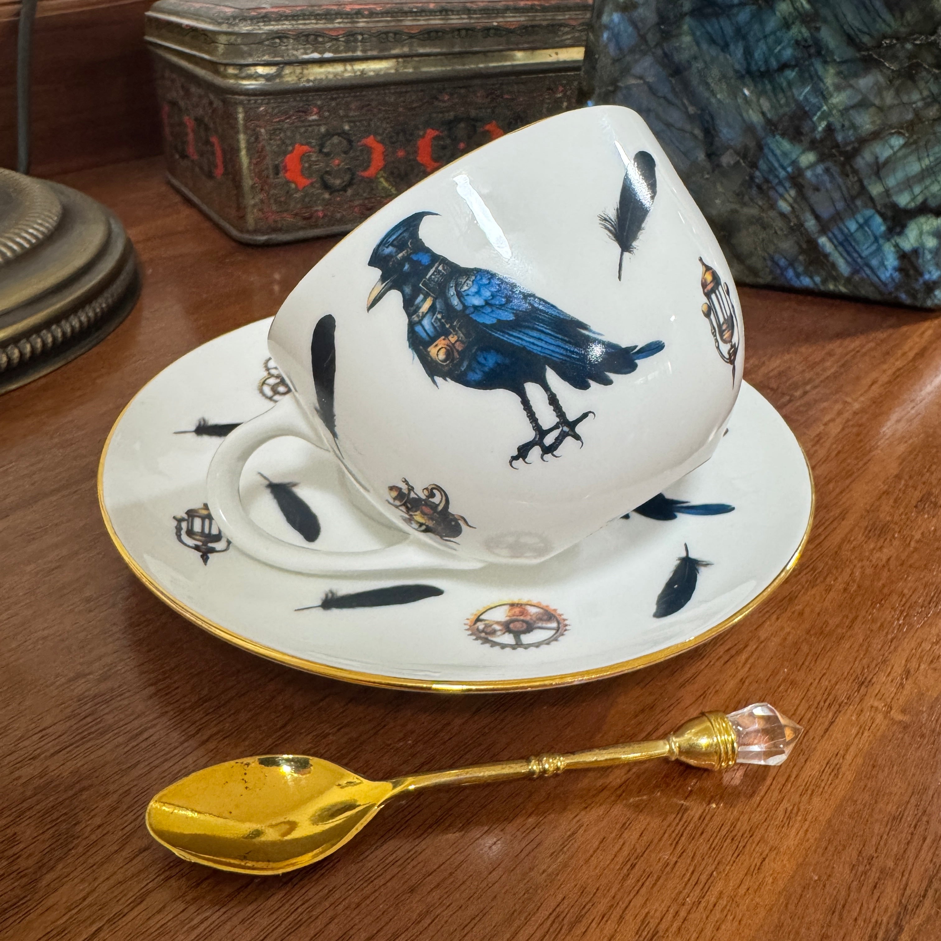 Cup and saucer with bird design on a wooden surface with a gold spoon.