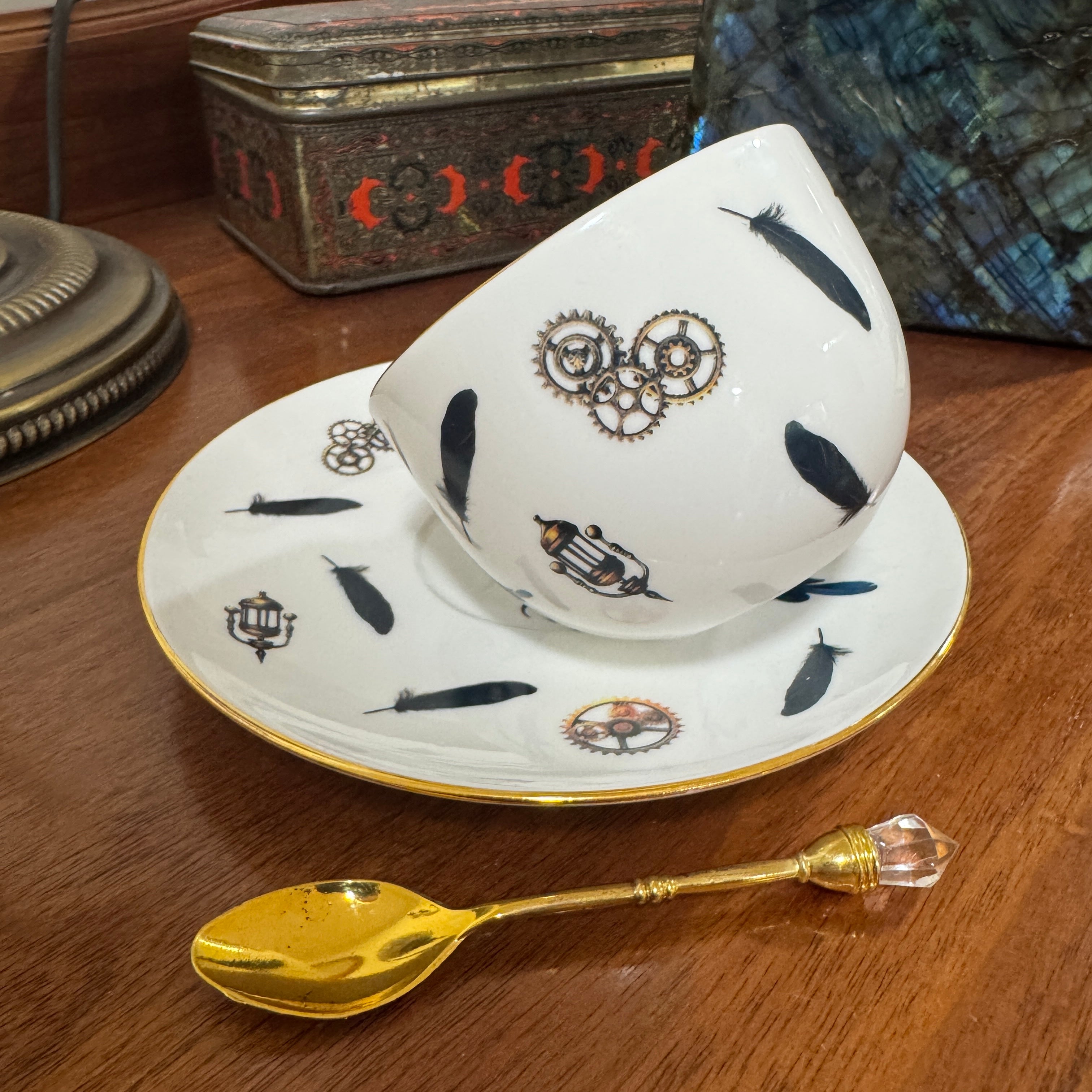 Teacup and saucer with decorative patterns on a wooden surface, accompanied by a gold spoon.