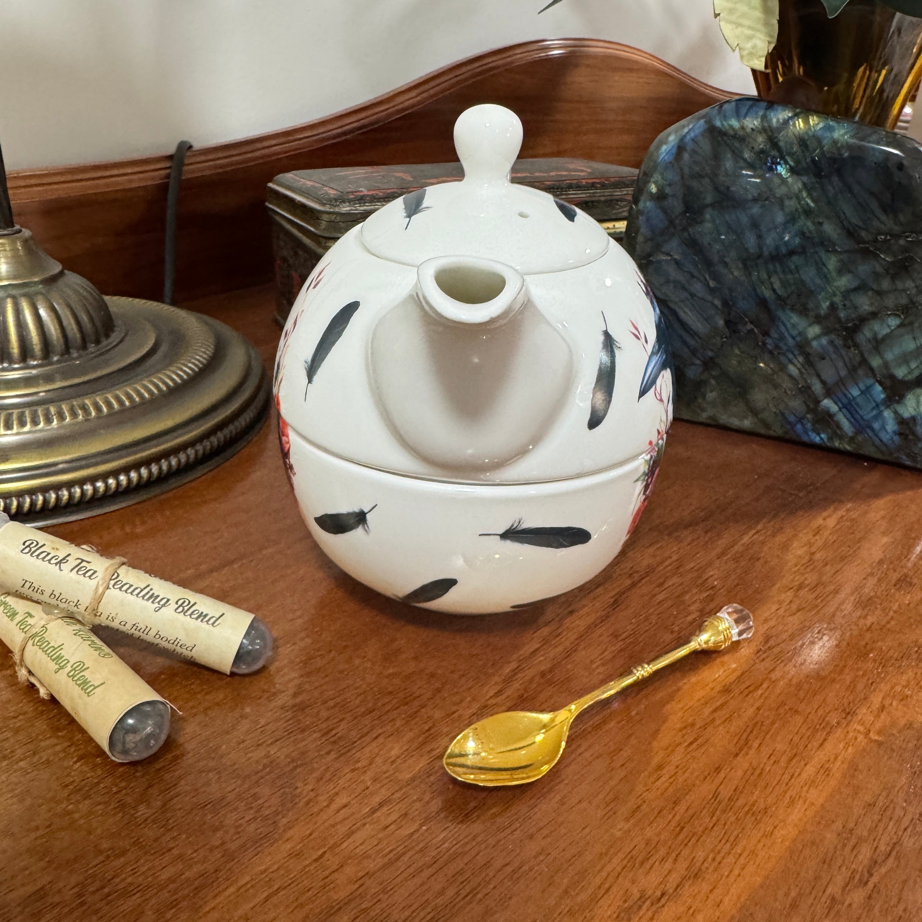 Decorative teapot with fish patterns on a wooden surface with a gold spoon and tea packaging.