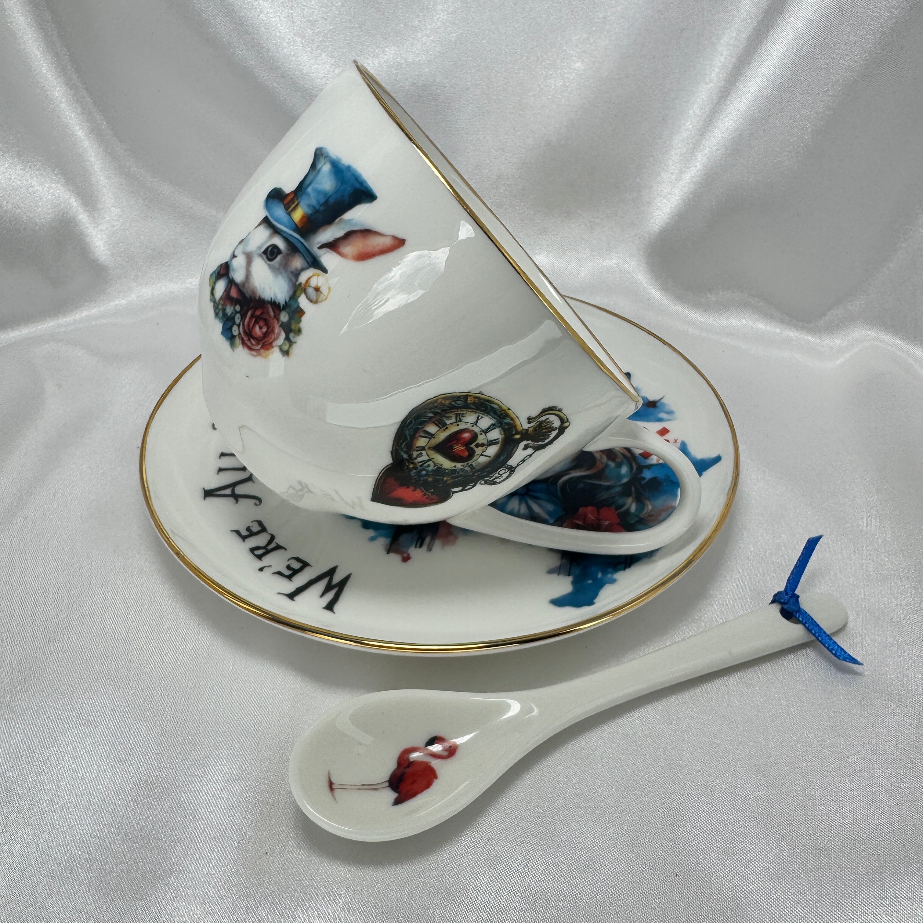 Decorative teacup, saucer, and spoon with artistic designs on a white fabric background