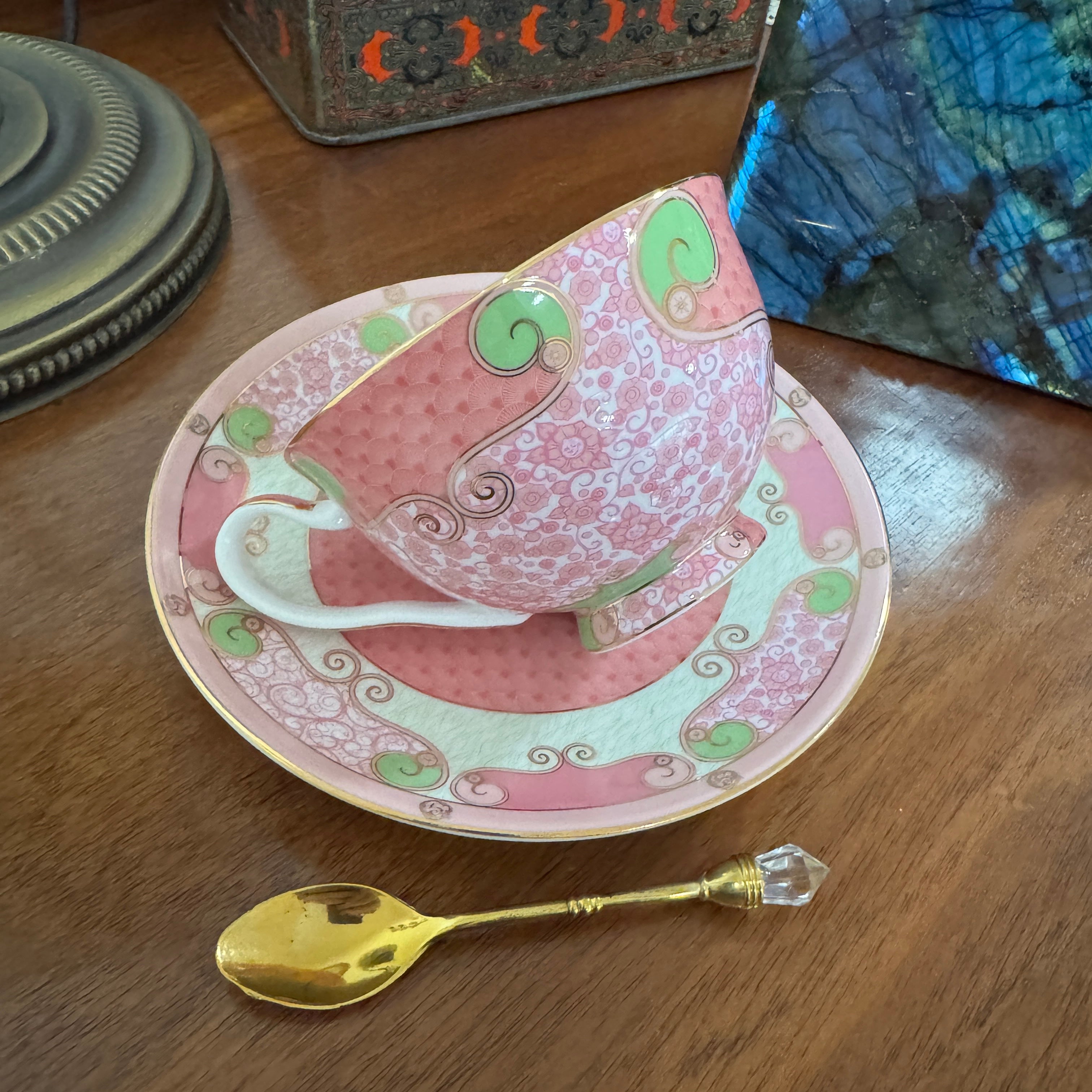Decorative pink teacup and saucer with a gold spoon on a wooden surface