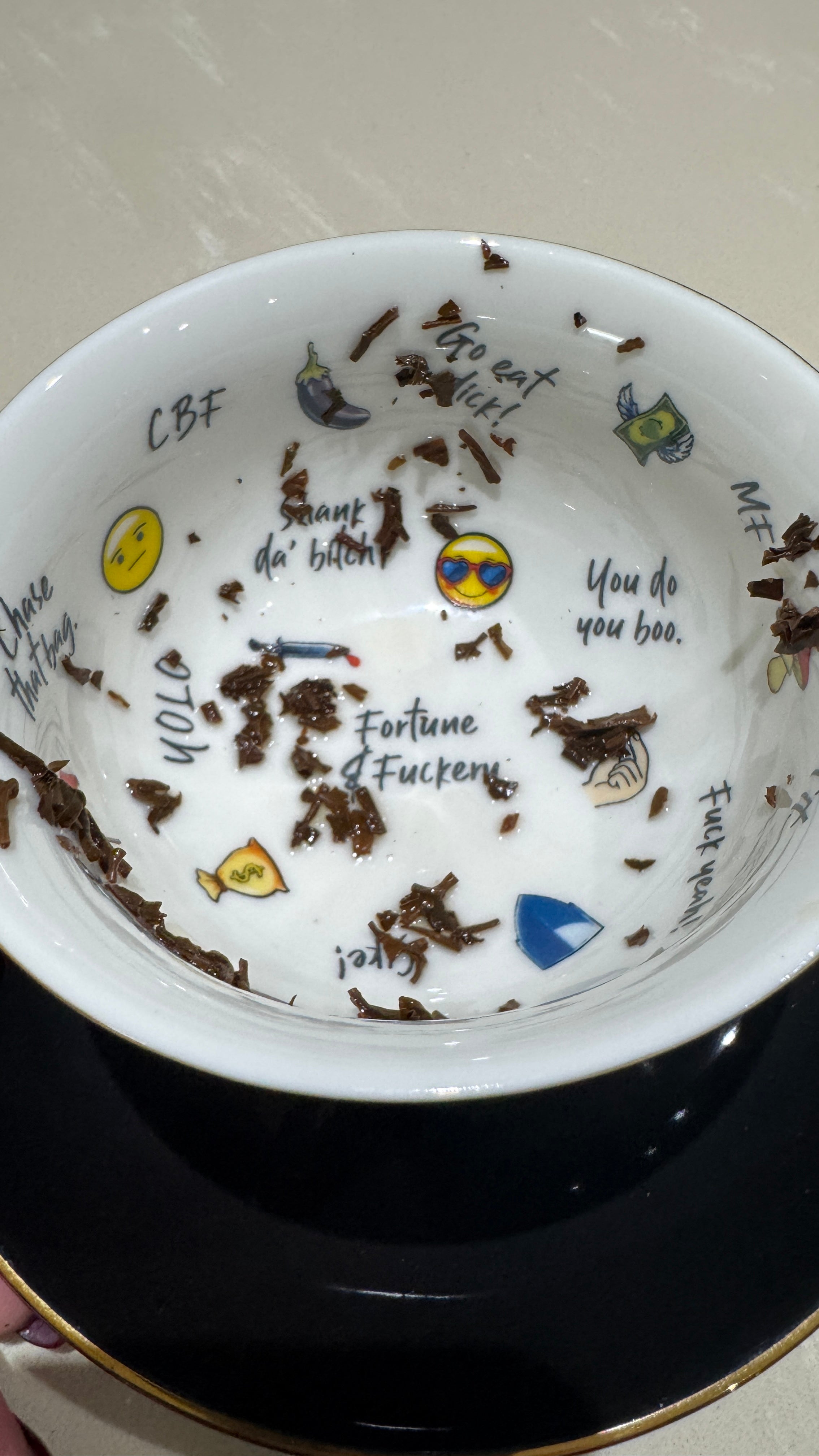 Teacup and saucer in black and gold with tea leaves pictured inside the teacup