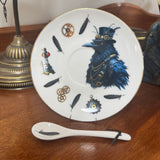 Decorative plate with a blue raven design and accessories on a wooden surface