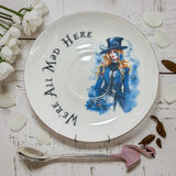 Steampunk Alice in a blue top hat and tailcoat on the saucer, with We're All Mad Here lettering curving around the rim