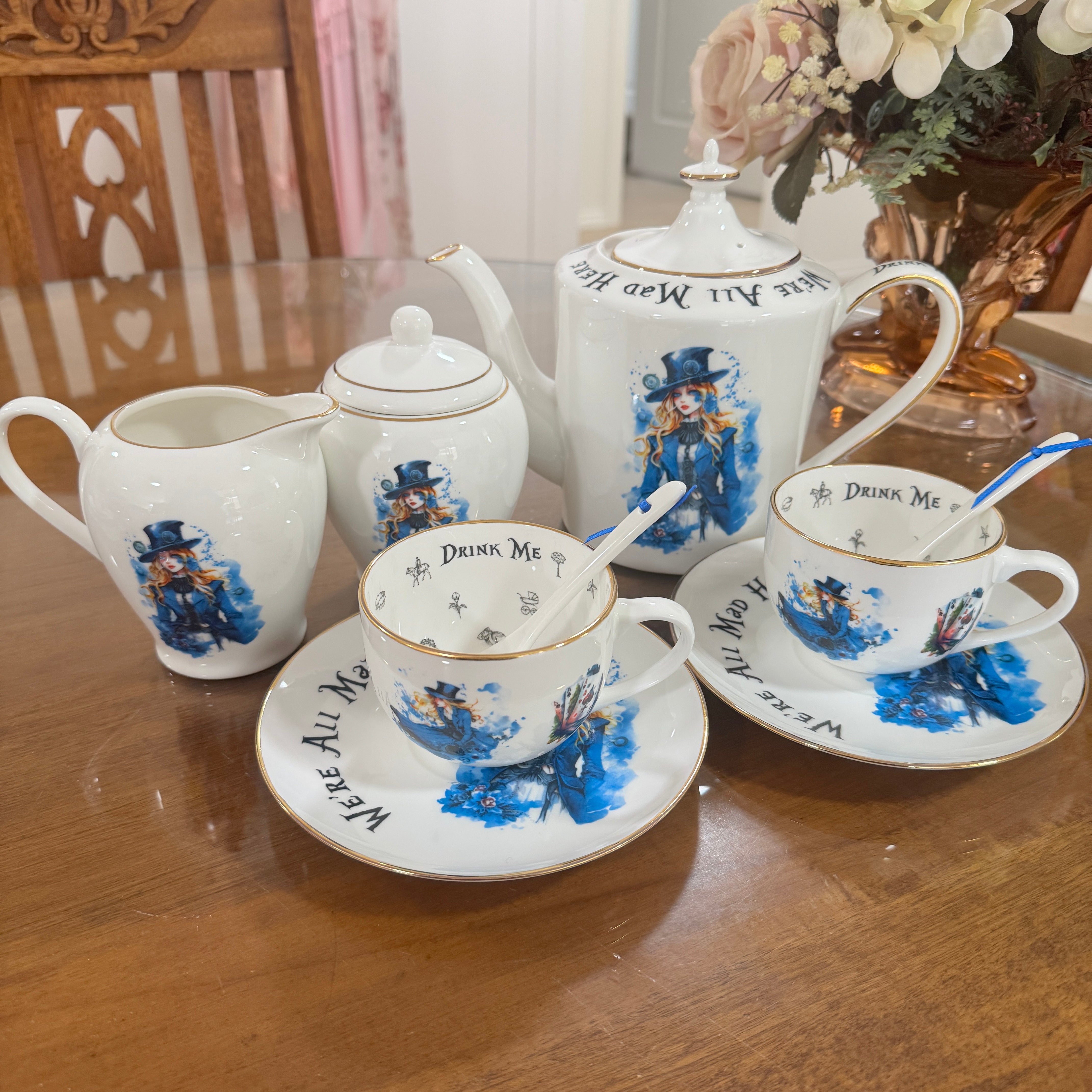 Tea set with 'Drink Me' text and blue floral designs on a wooden table.