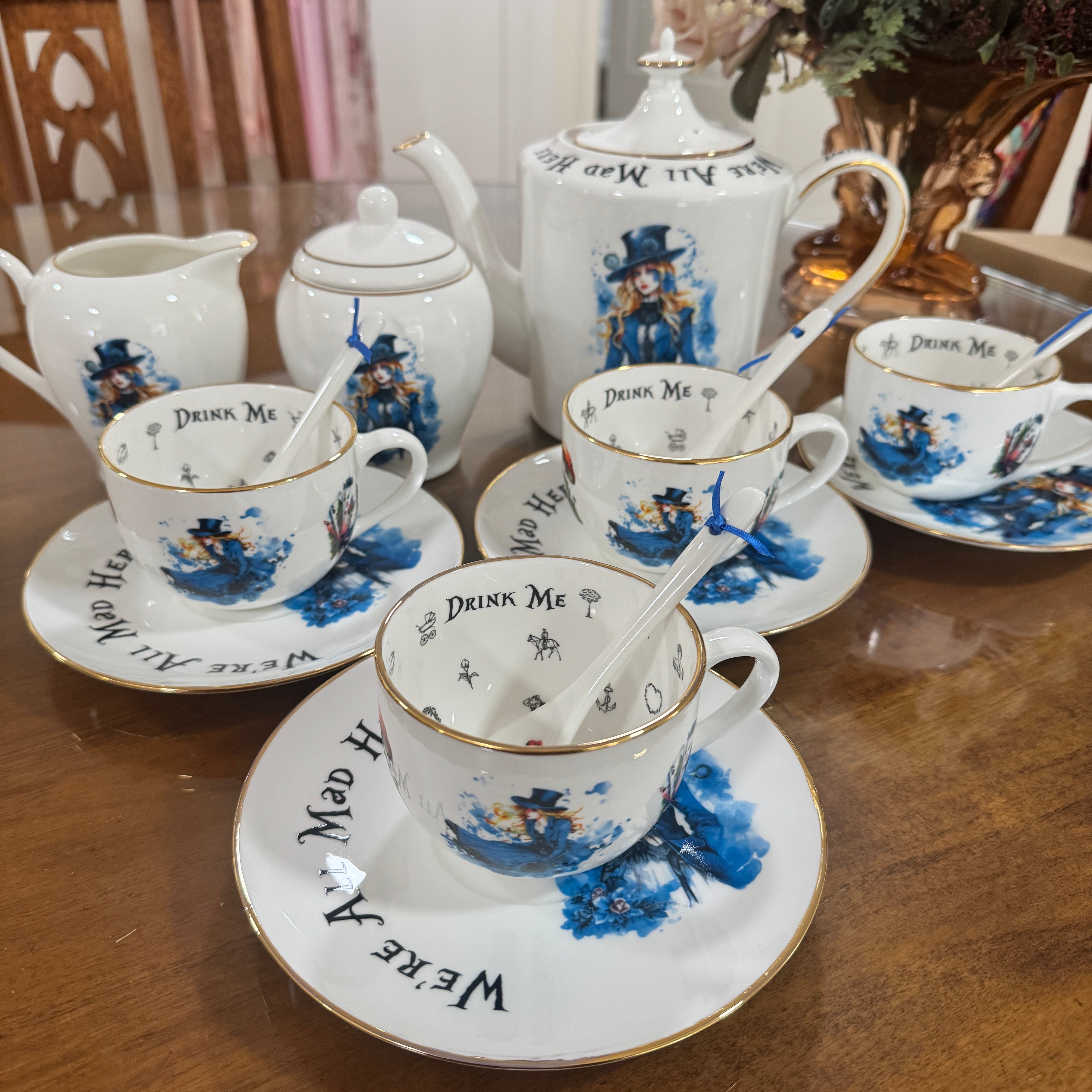 Tea set with 'Drink Me' and 'Where Are We' text on a wooden table.