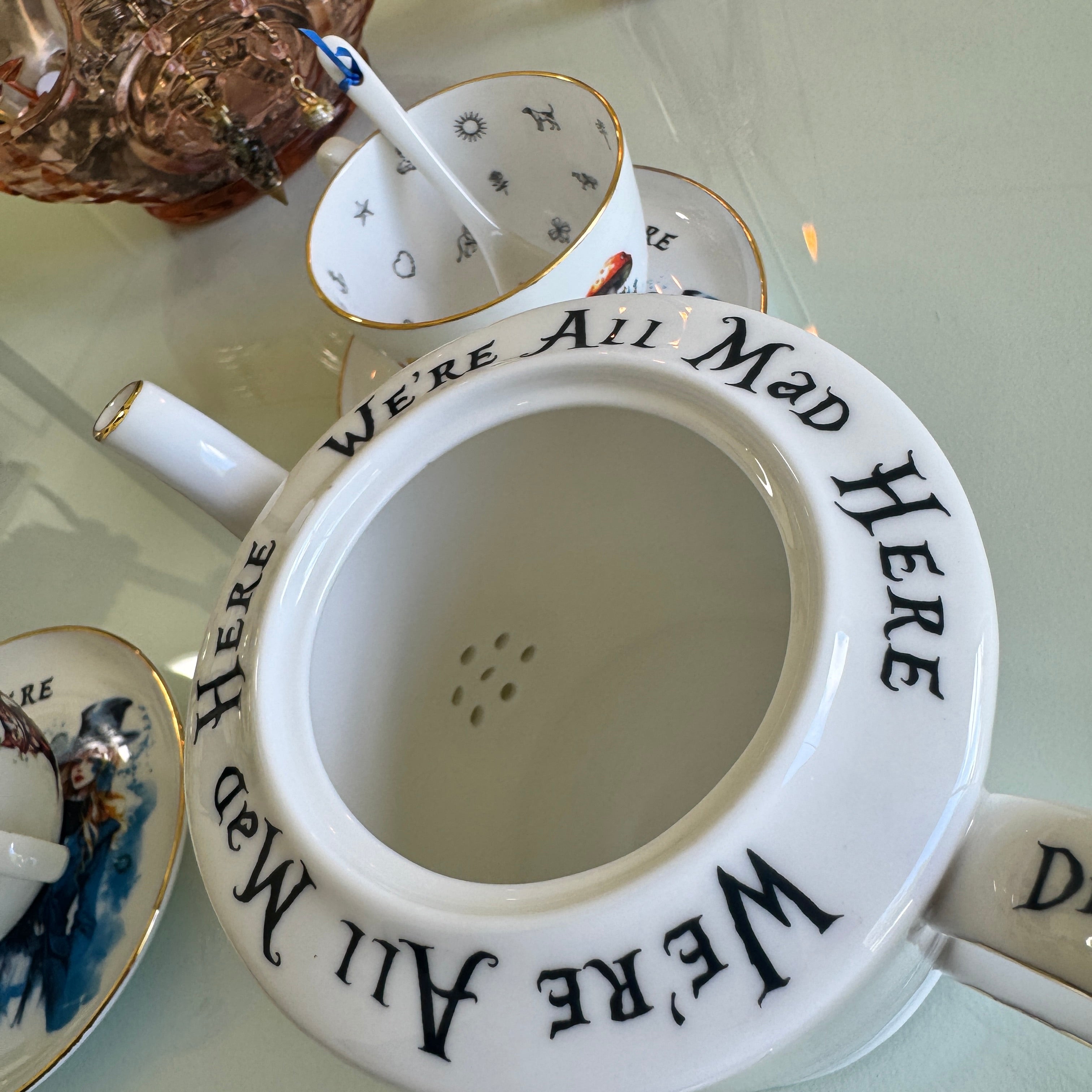 White teapot with 'We're All Mad Here' text on a reflective surface