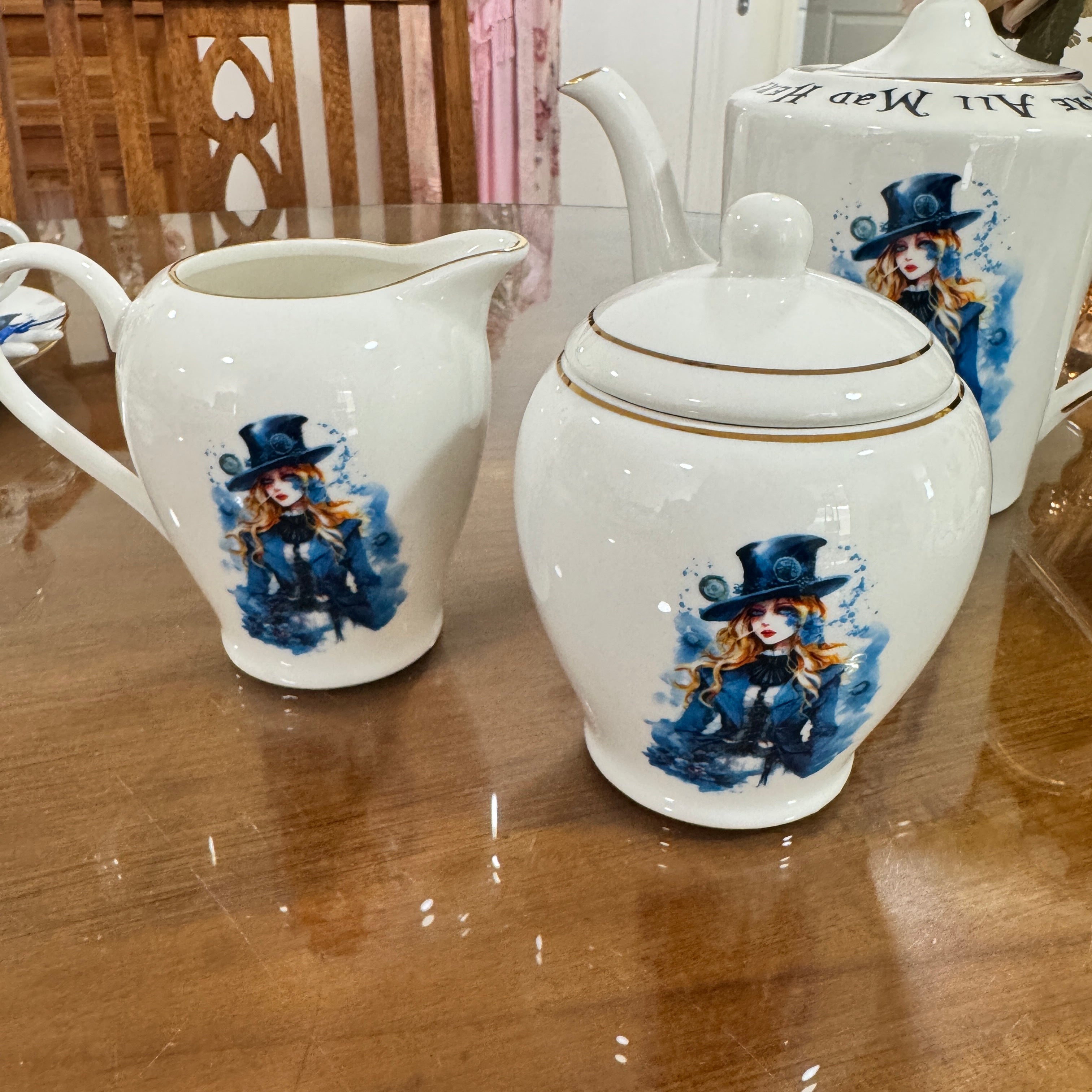 White ceramic sugar and creamer with decorative figures on a wooden table.