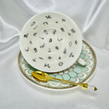 Elegant porcelain cup on its side showing internal symbols for tea leaf reading, resting on a matching saucer with a gold spoon.