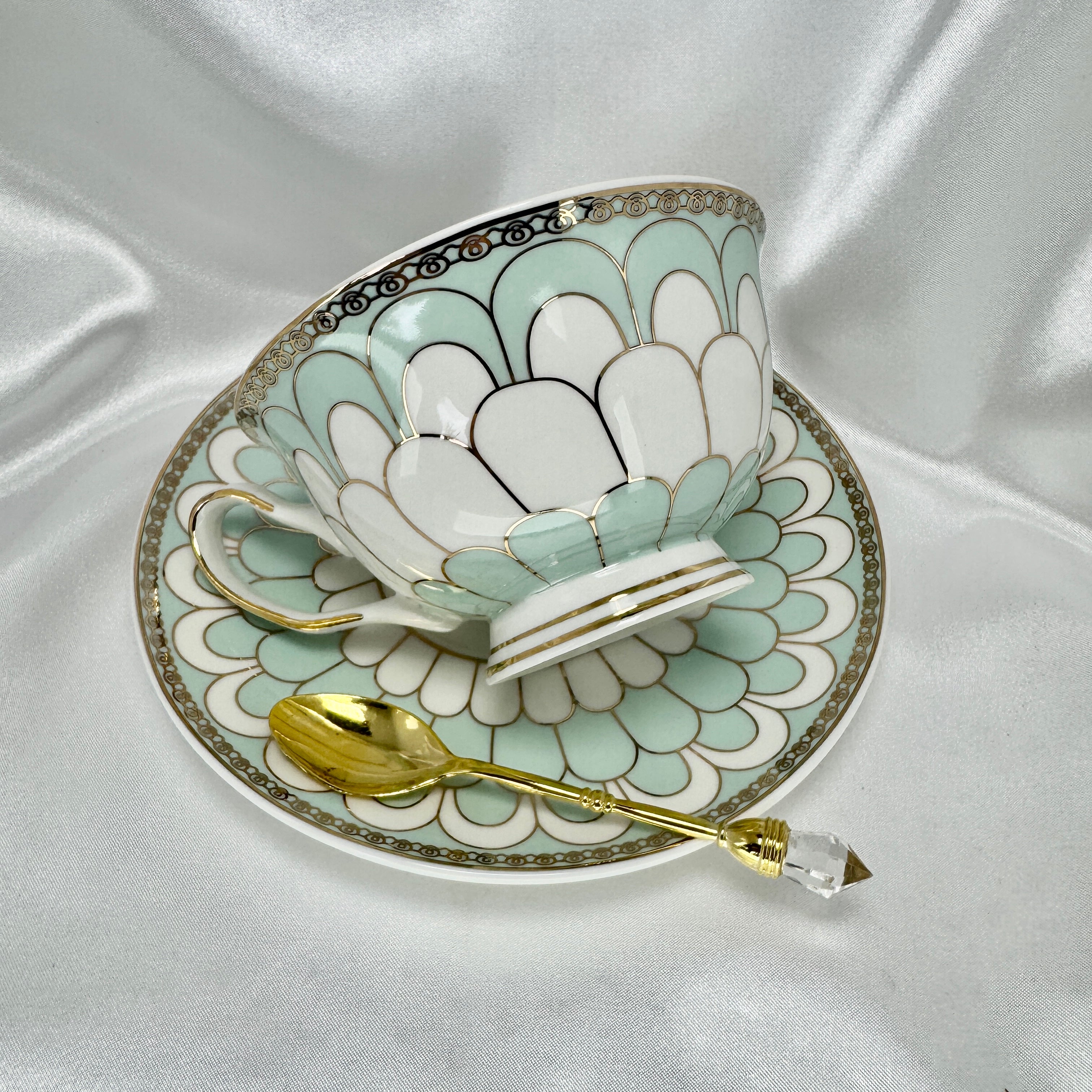 Left side view of the tea cup and saucer, showing internal tea leaf reading symbols and a gold spoon resting inside.