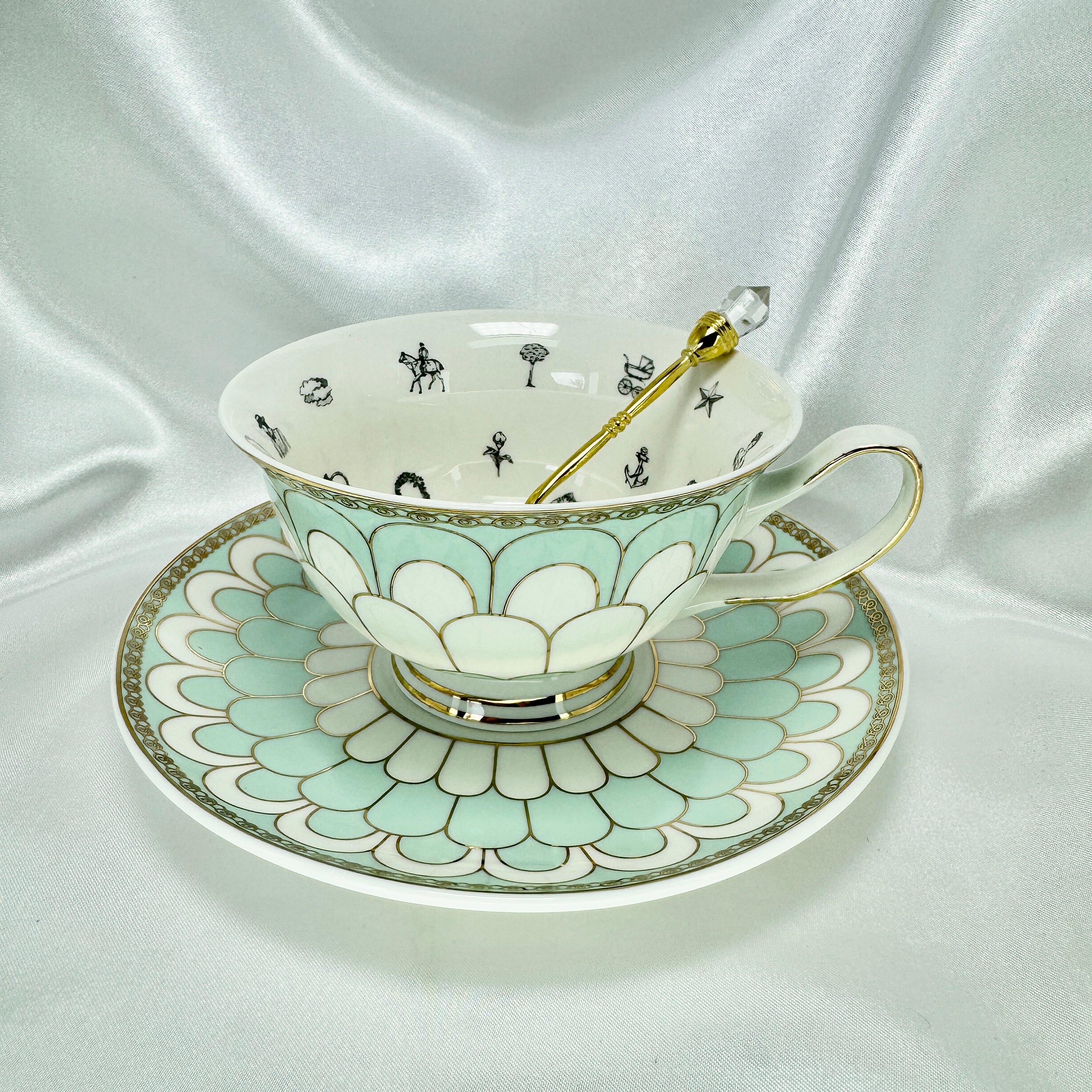 Overhead view of the porcelain teacup with black fortune telling symbols inside, sitting on the patterned saucer with a gold spoon.