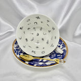 Blue and white teacup and saucer set with gold trim, cup tilted on its side showing tiny black divination symbols inside.