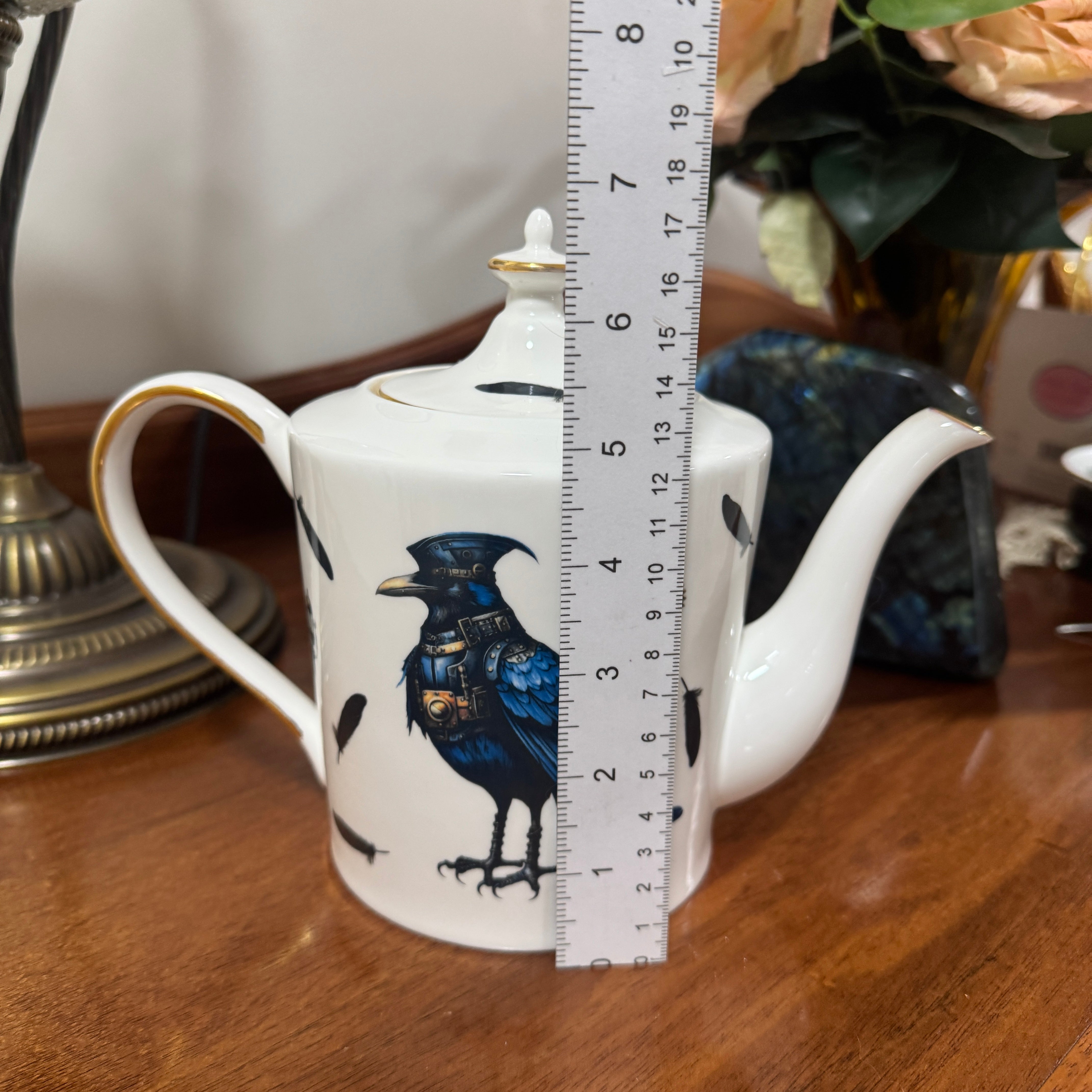 Teapot with bird design and ruler for scale on a wooden surface