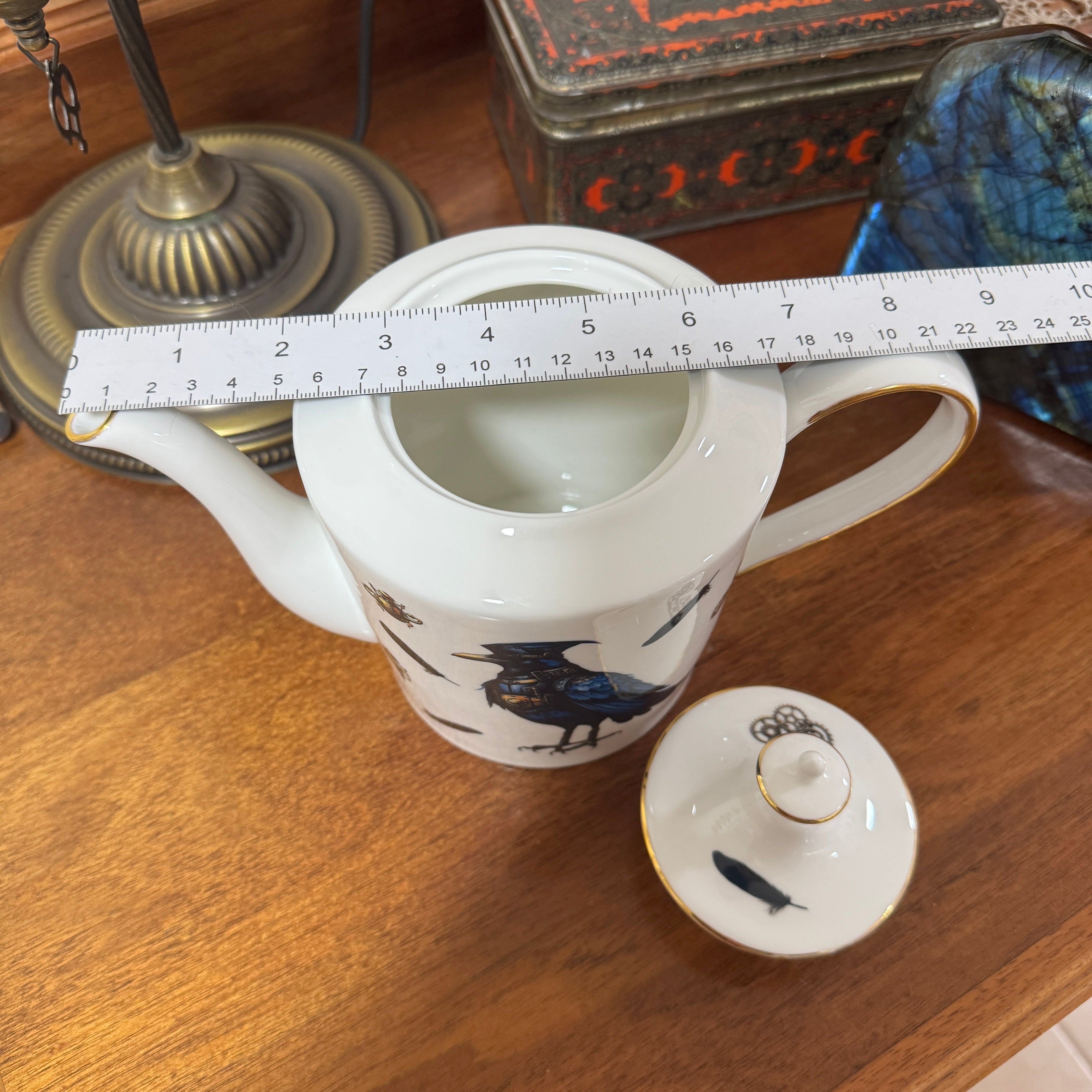 White teapot with decorative elements on a wooden surface, measured by a ruler.
