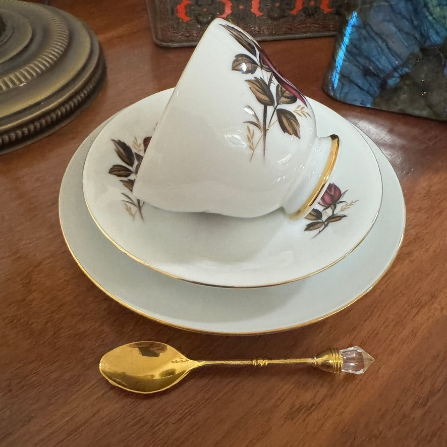Decorative teacup and saucer with floral patterns on a wooden table, accompanied by a gold spoon.
