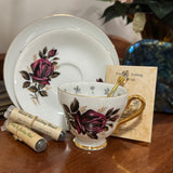 Teacup with floral design on a wooden surface, accompanied by a saucer and black tea packaging.