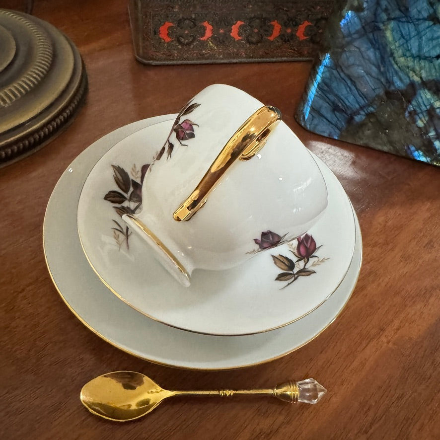 Teacup and saucer set with floral design and gold accents on a wooden surface.