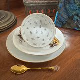 Tea cup, saucer, and spoon on a wooden surface with decorative elements.