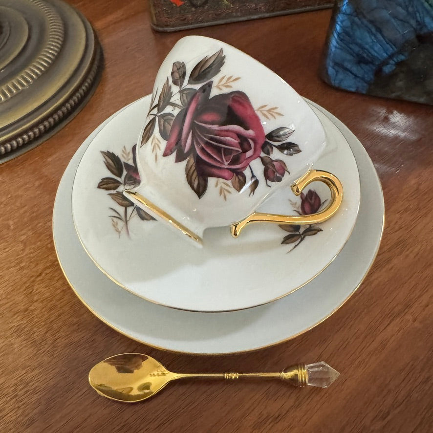 Decorative teacup with floral design and gold handle on a wooden surface with a spoon.