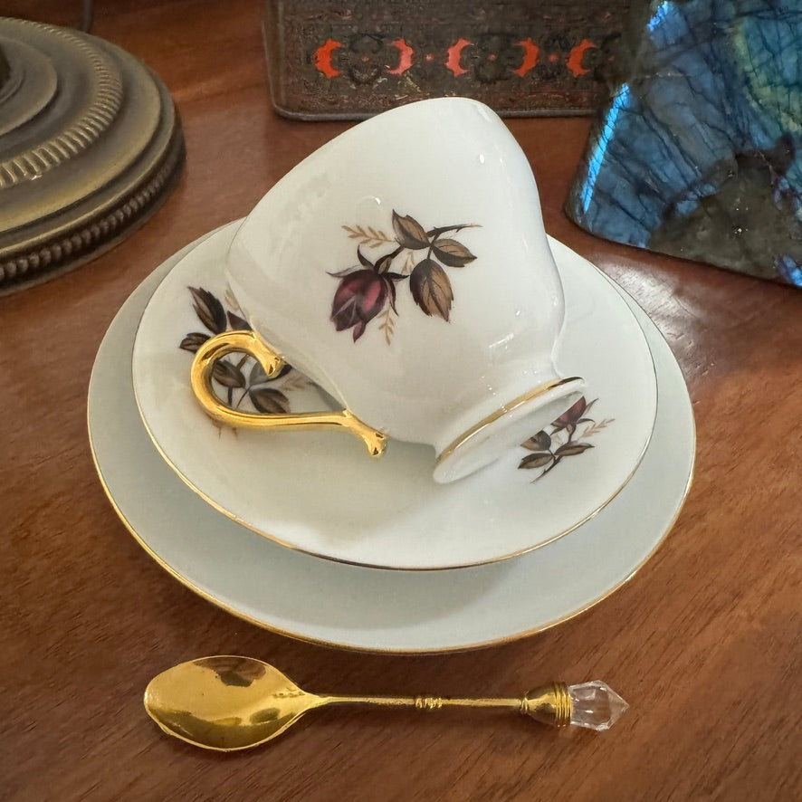 Teacup with floral design on a saucer with a gold handle, placed on a wooden surface with a decorative spoon.