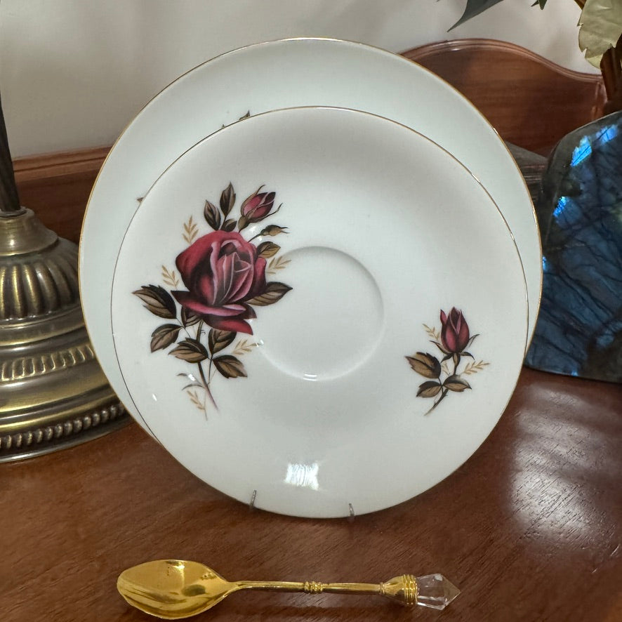 Decorative saucer with floral design on a wooden surface next to a gold spoon.