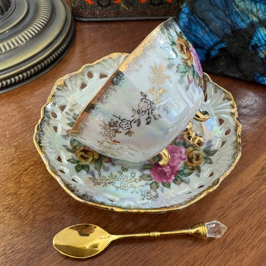 Decorative teacup and saucer with floral patterns on a wooden surface, accompanied by a gold spoon.