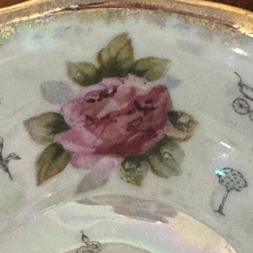 Close-up of a ceramic plate with a painted pink rose and green leaves.