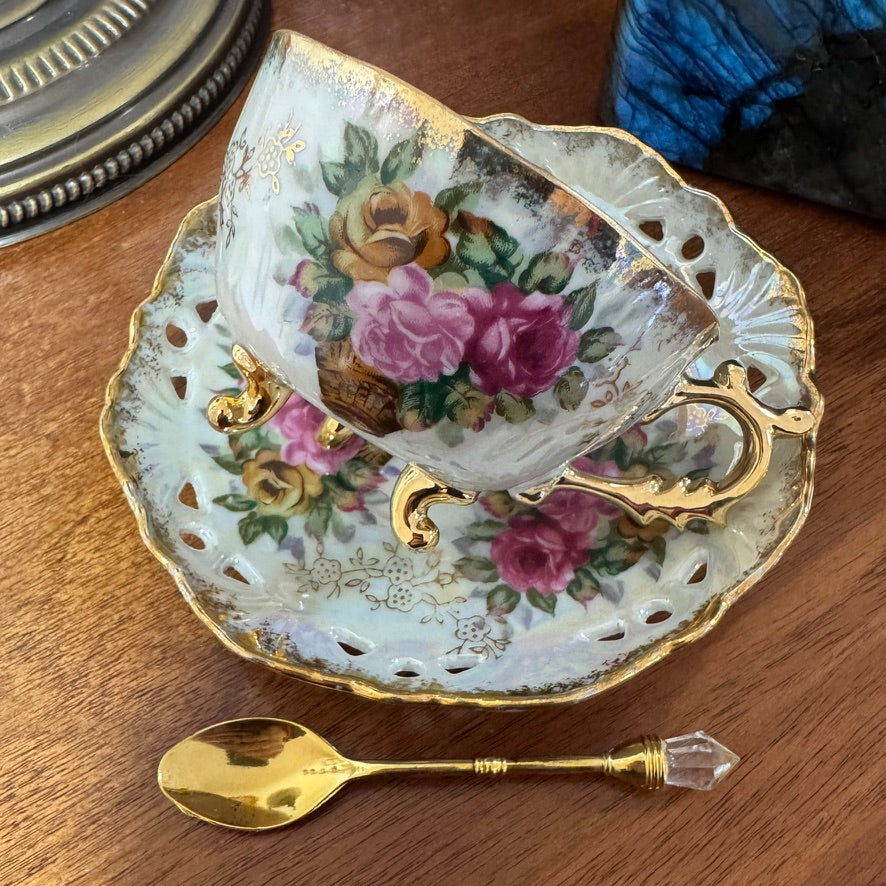 Decorative teacup and saucer with floral patterns on a wooden surface, accompanied by a gold spoon.