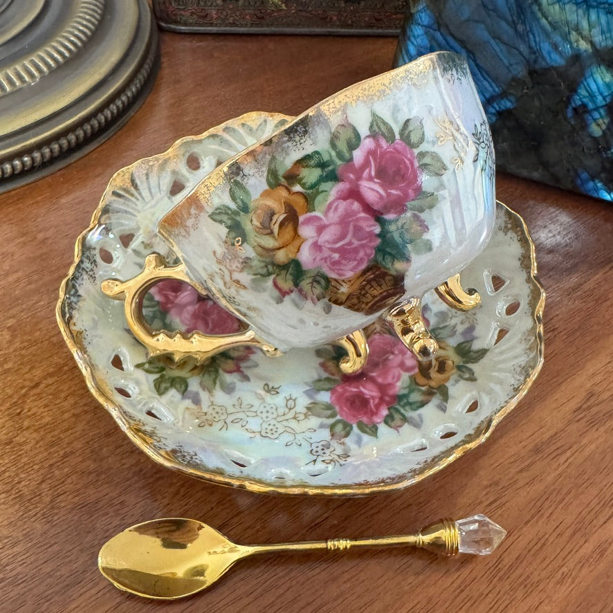 Decorative teacup and saucer with floral design on a wooden surface, accompanied by a gold spoon.