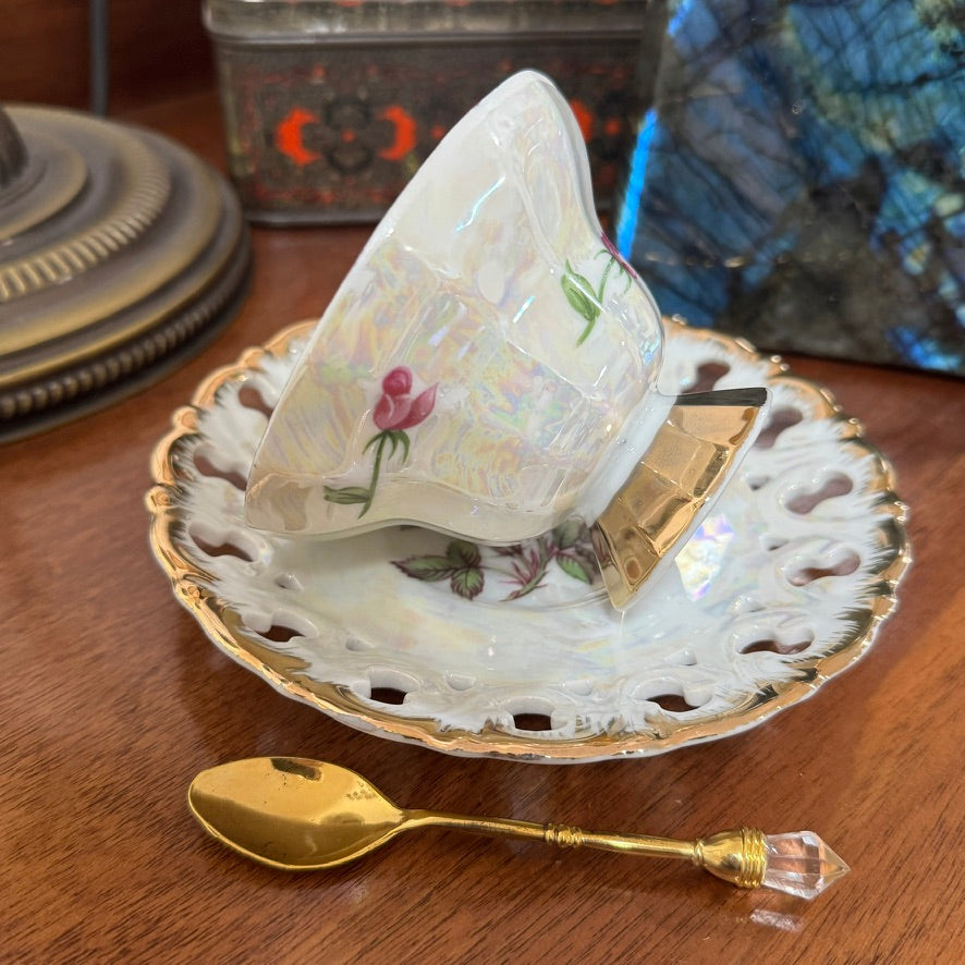 Teacup with floral design on a saucer with a gold spoon on a wooden surface