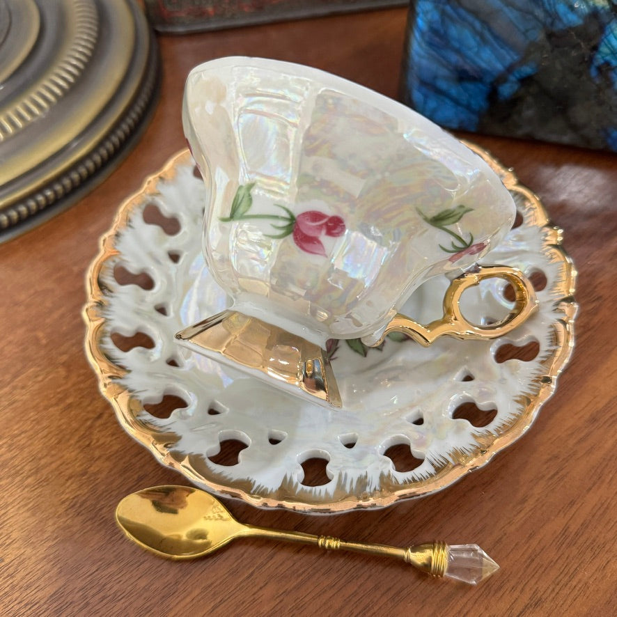 Vintage-style teacup with floral design on a matching saucer, accompanied by a gold spoon on a wooden surface.