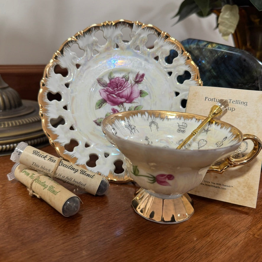 Vintage-style teacup with gold trim and floral design on a wooden surface, next to decorative plates and tea bags.
