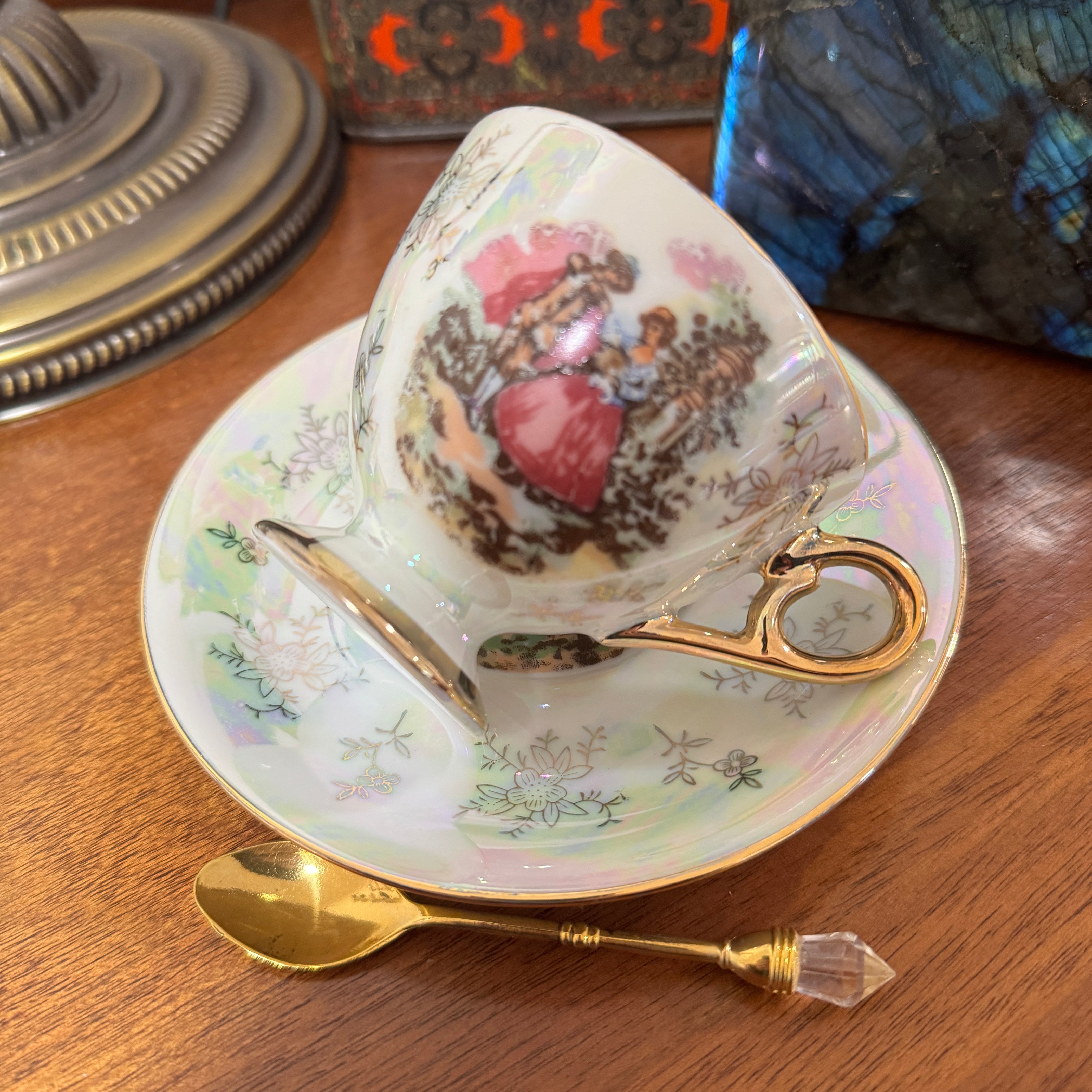 Decorative teacup with floral design on a saucer with a spoon, all on a wooden surface.