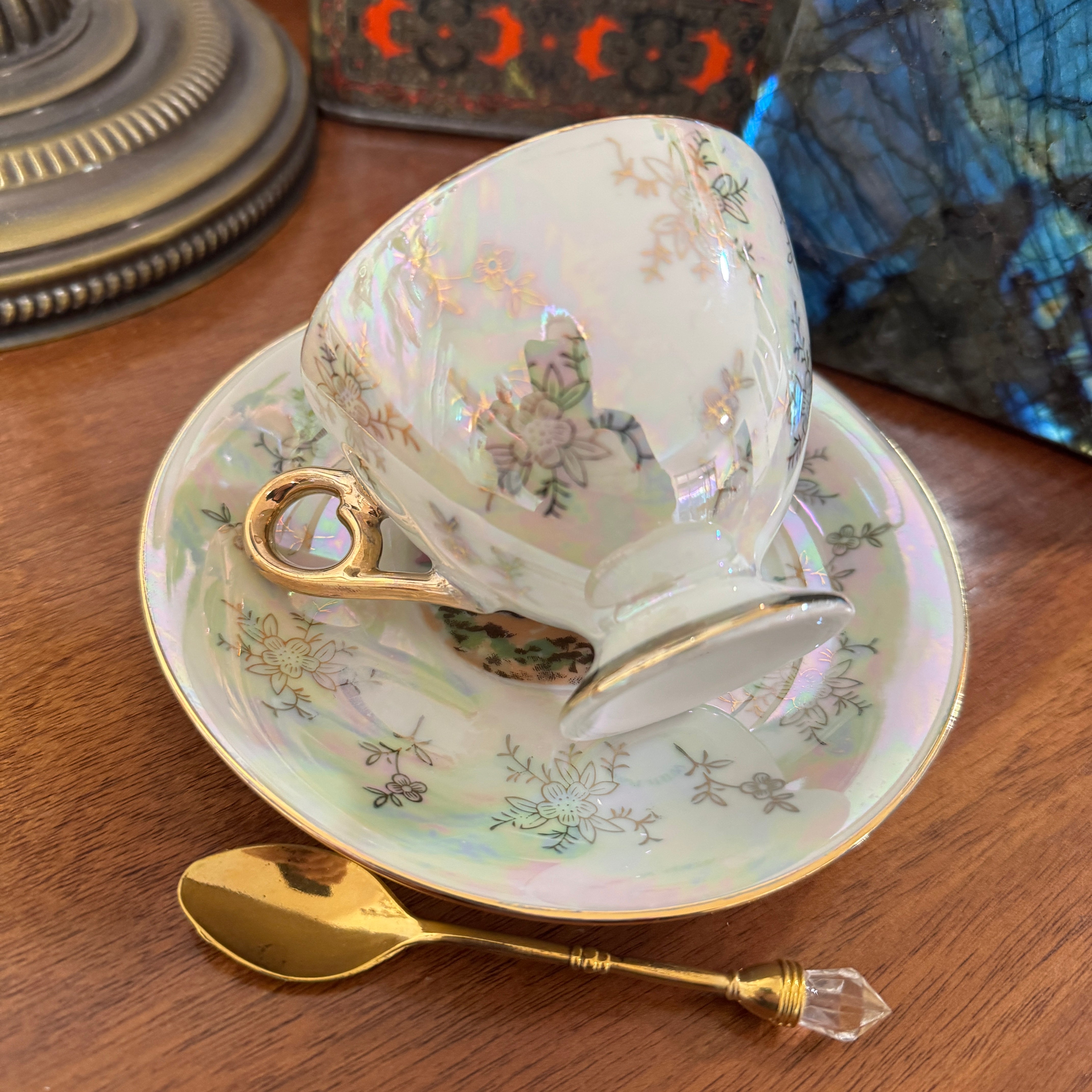 Teacup with floral design on a saucer with a gold spoon on a wooden surface