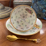 Teacup with decorative interior, saucer, and gold spoon on a wooden surface