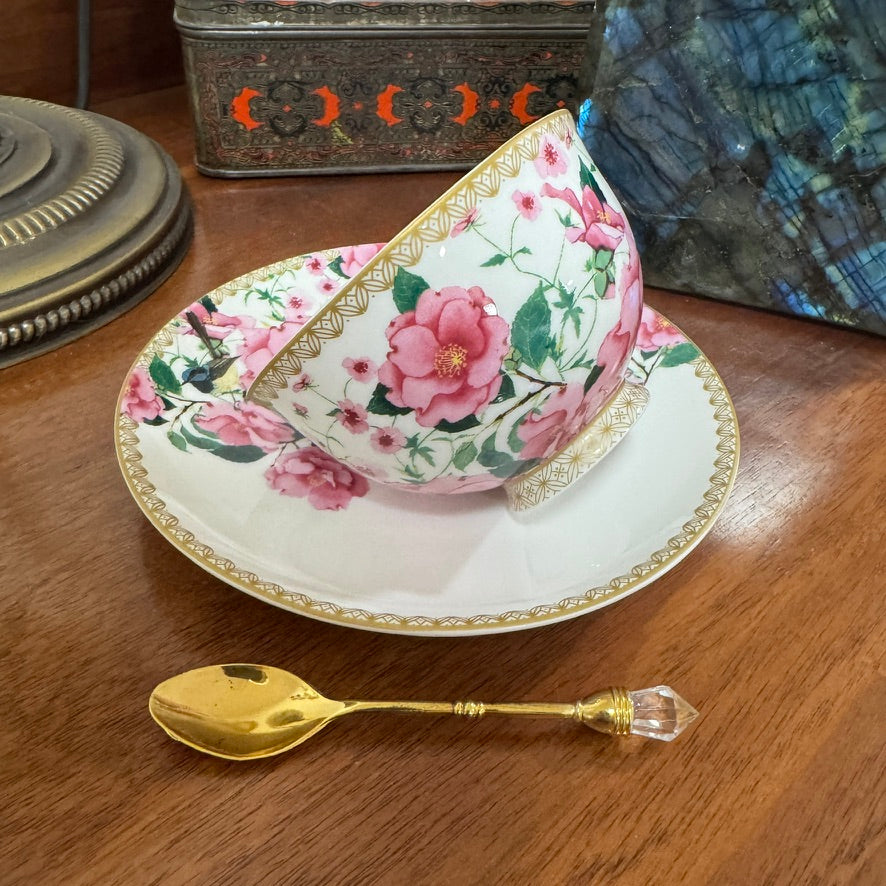 Floral teacup and saucer set on a wooden surface with a gold spoon.