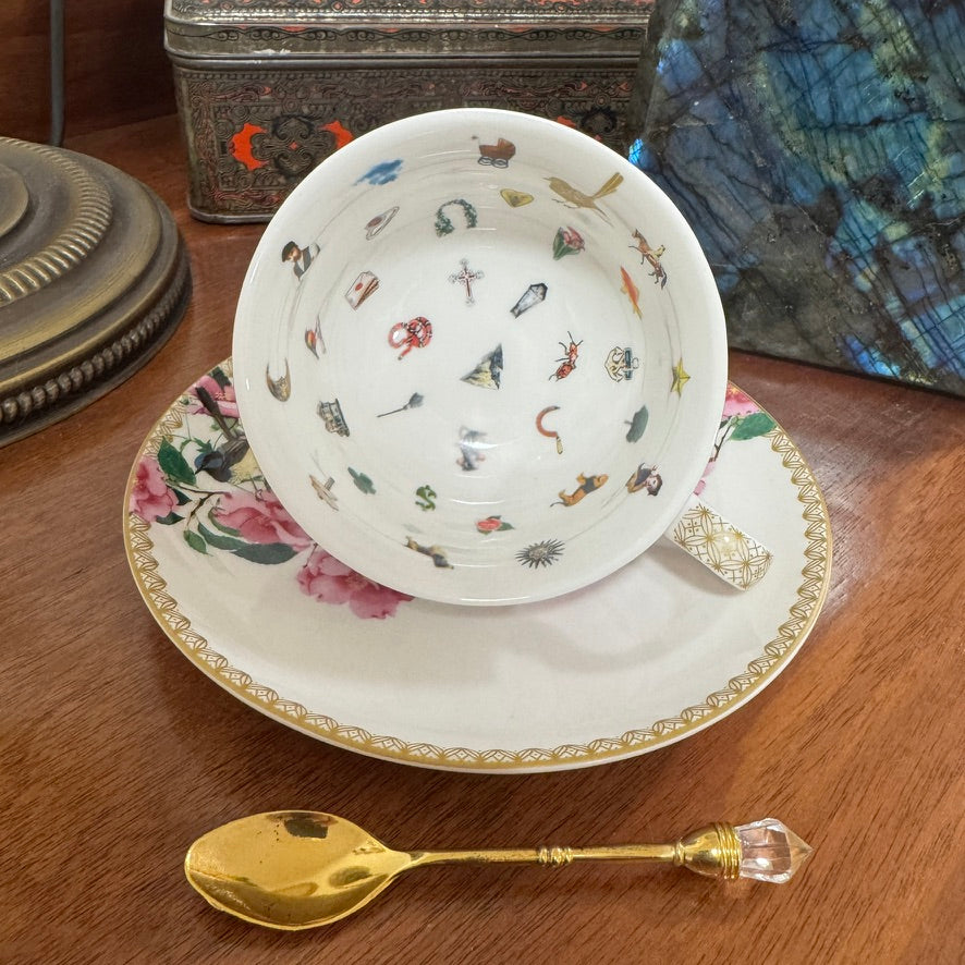 Teacup with decorative interior, saucer, and gold spoon on a wooden surface