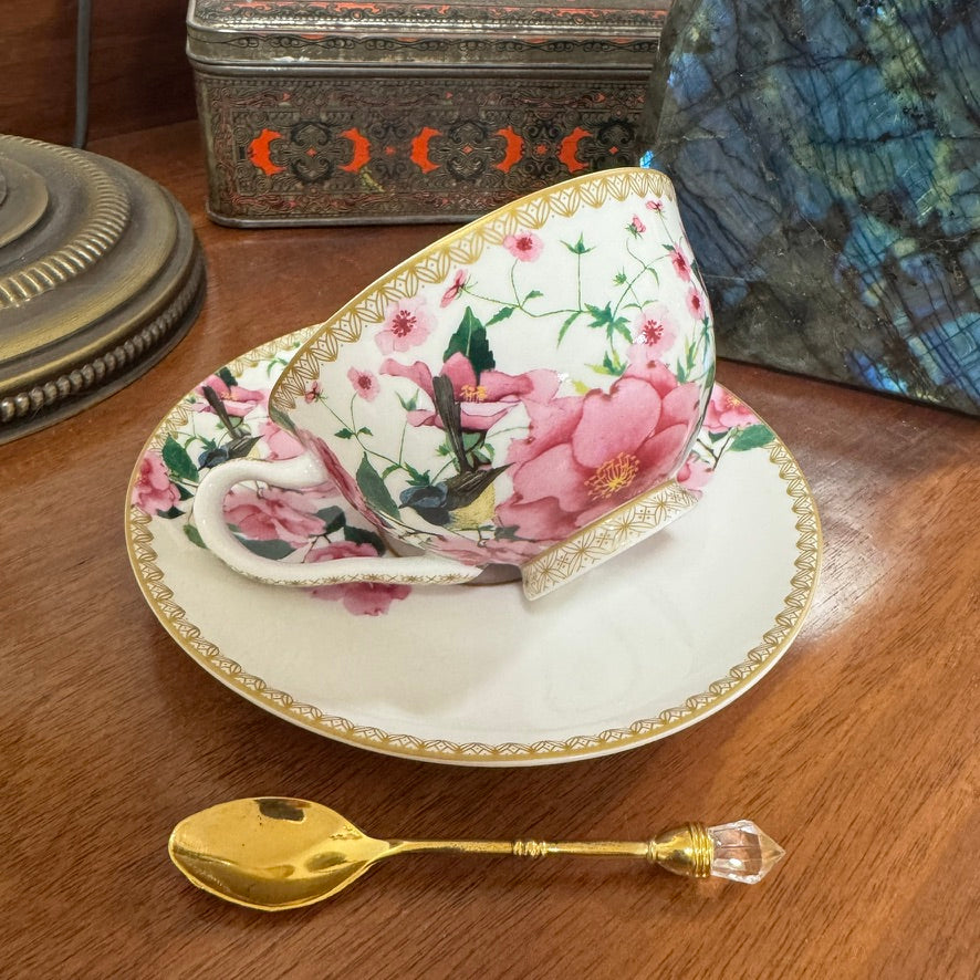 Floral teacup and saucer set on a wooden surface with a gold spoon.