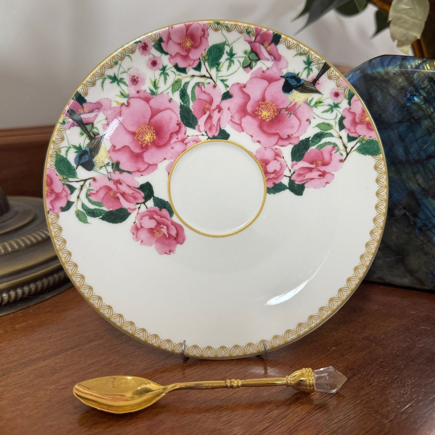 Floral plate with pink roses and gold accents on a wooden surface with a spoon.