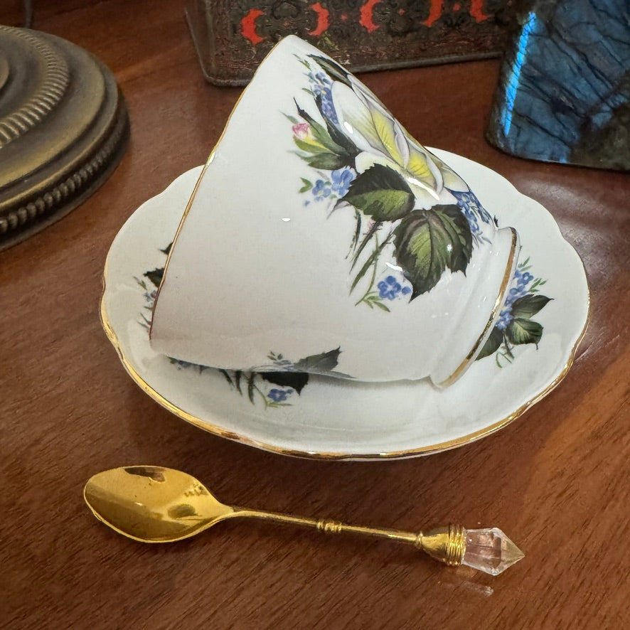 Teacup with floral design on a saucer with a gold spoon on a wooden surface