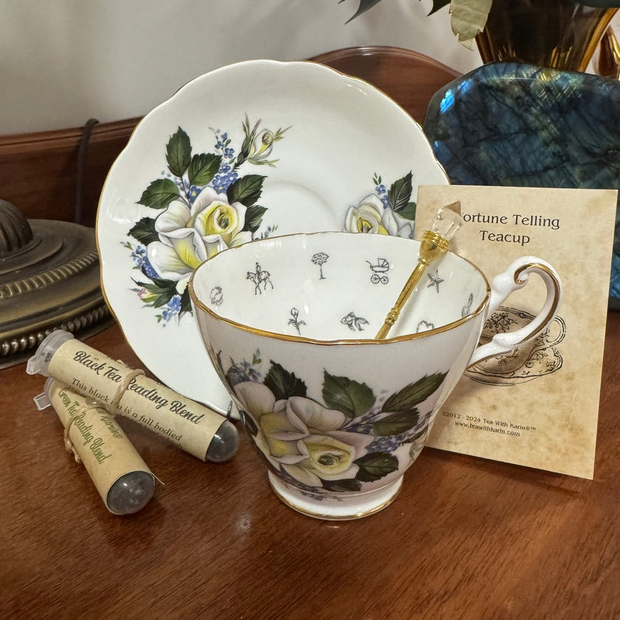 Decorative teacup with floral design on a wooden surface, accompanied by tea leaves and a card.