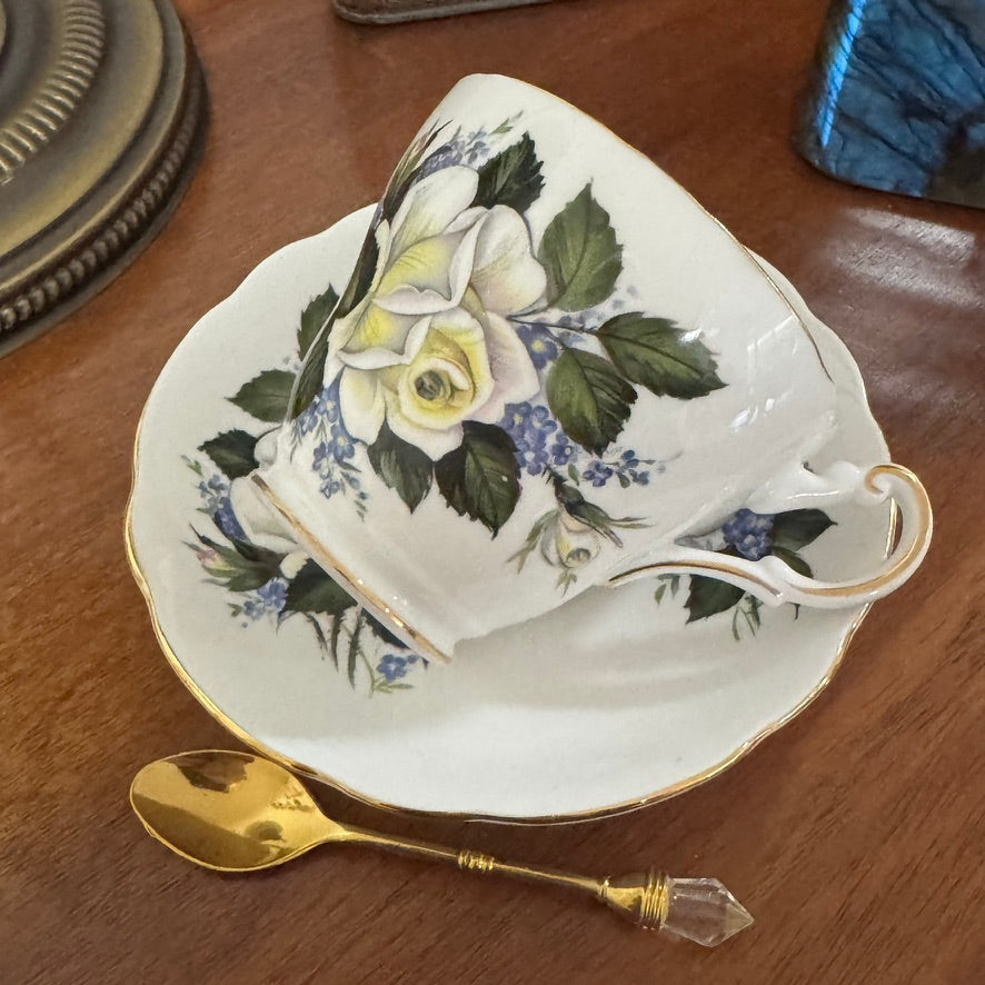 Floral teacup and saucer set with a gold spoon on a wooden surface