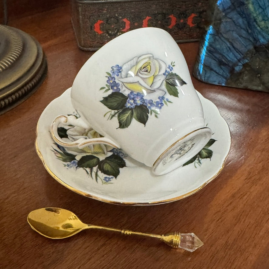 Teacup with floral design on a saucer and gold spoon on a wooden surface