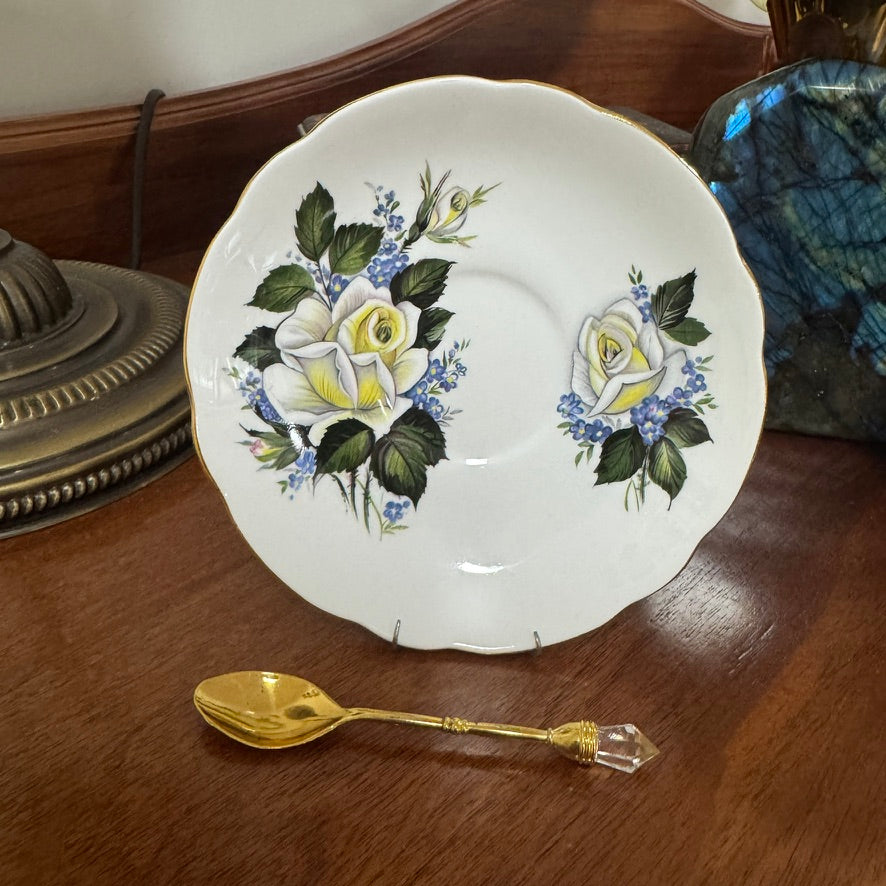 Decorative plate with floral design on a wooden surface next to a gold spoon.