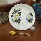 Decorative plate with floral design on a wooden surface next to a gold spoon.
