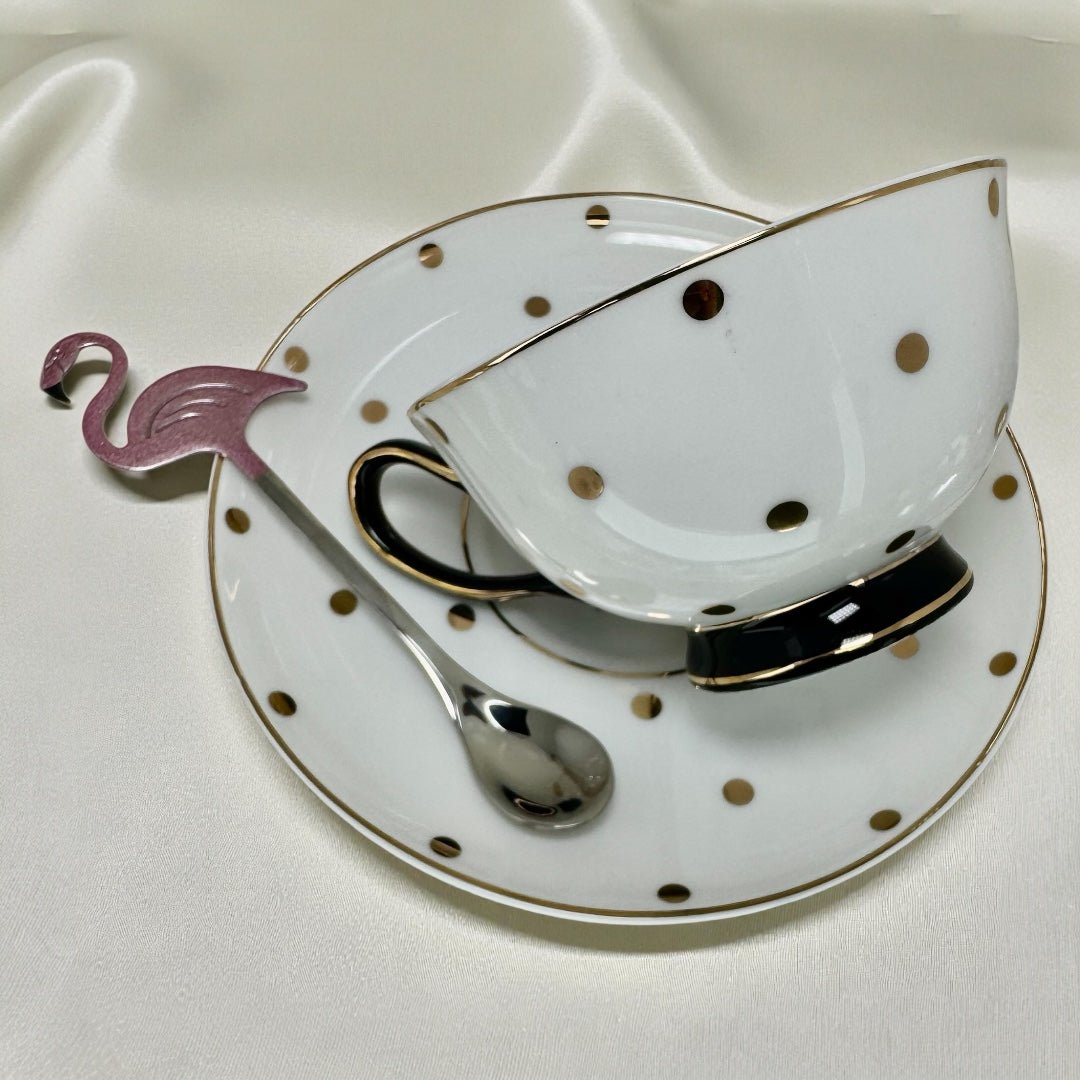 Black and gold polka dot new bone china tea cup and saucer set. The cup has a black base and handle, gold rim, and is shown with a pink flamingo spoon resting on the saucer.