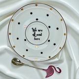 New bone china tea saucer with gold and black polka dots, featuring the quote 'We are all mad here' in the center. Shown next to a polished silver spoon and a decorative pink flamingo handle.
