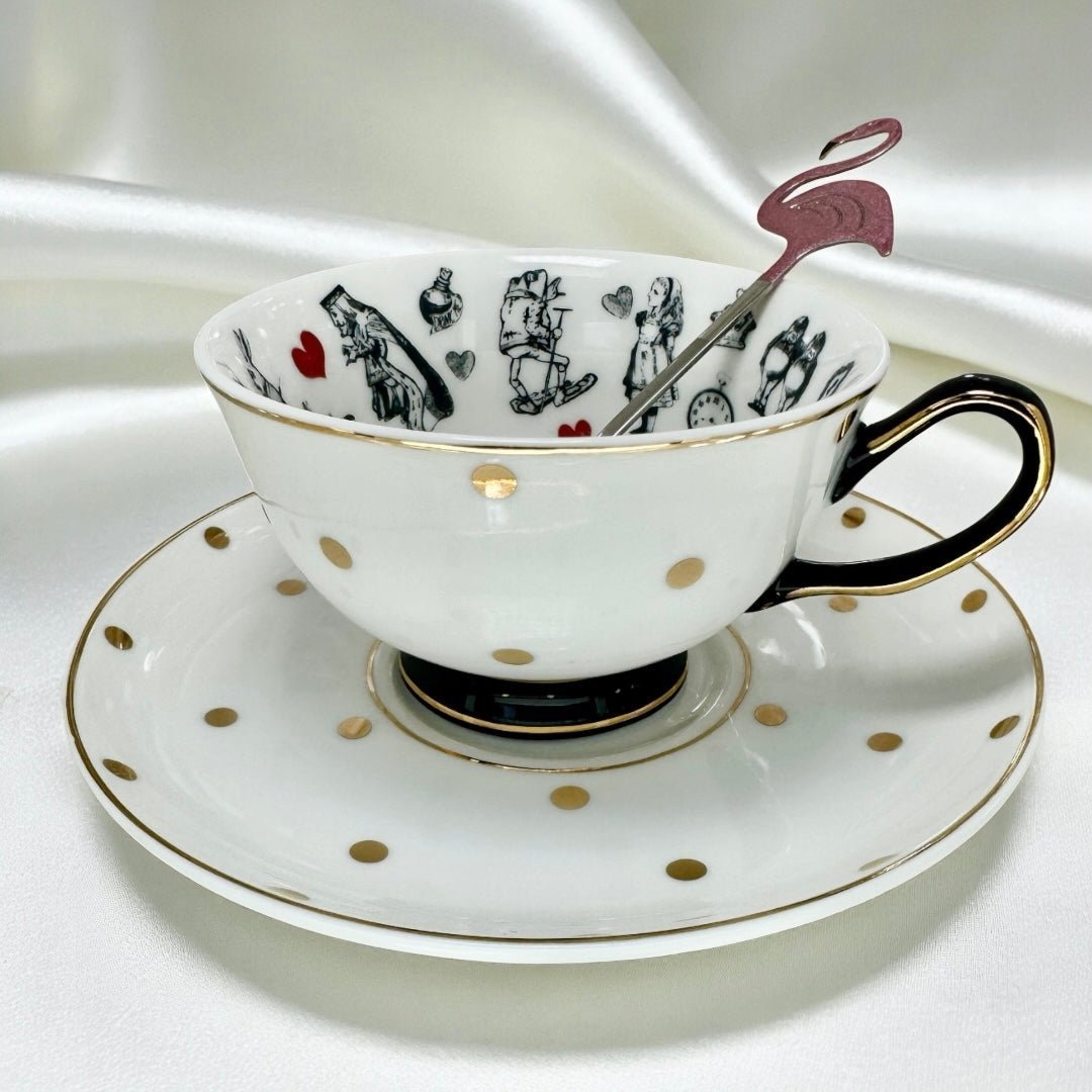 Alice in Wonderland character print tea cup on a black and gold polka dot saucer. The cup features a black handle and base with gold accents, and a pink flamingo spoon